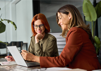 Two women talk in front of a laptop. 