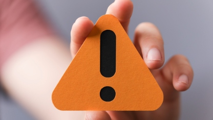 A sign of the exclamation mark on a yellow paper in the hands of a man