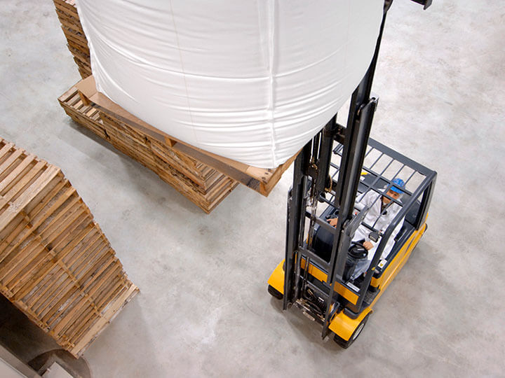 Aerial view of man in white jump suit and blue hard hat, driving a Battery-powered forklift truck in packaging warehouse