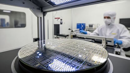 Technician in lab suit working with silicon wafer in a cleanroom with bright lighting. 