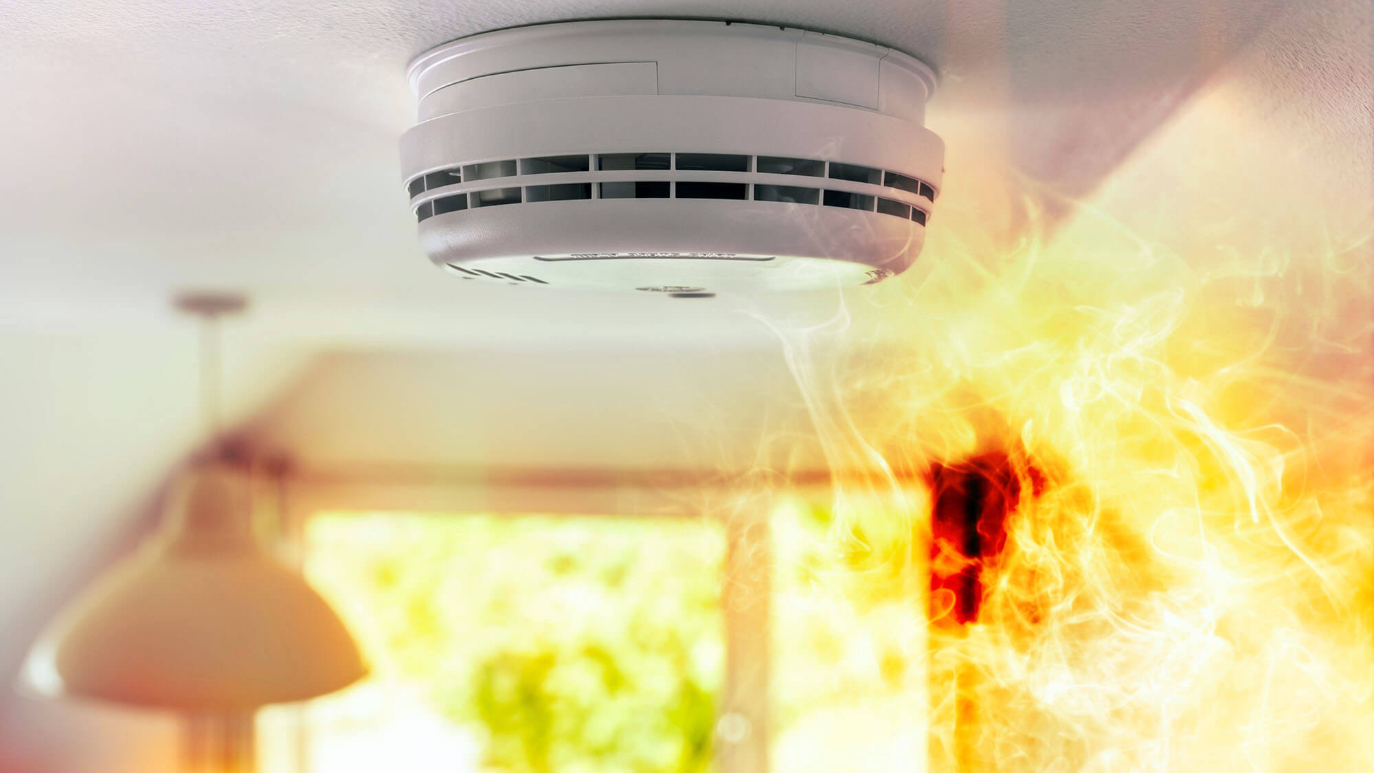 Smoke detector and interlinked fire alarm on ceiling in action background
